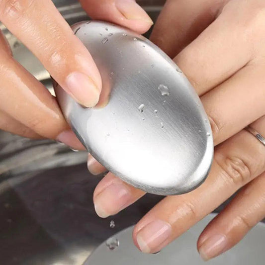 A person holds the Odor Remover Hand Bar Stainless Steel Soap under running water, using it to wash their fingers; water droplets are visible on the bar.