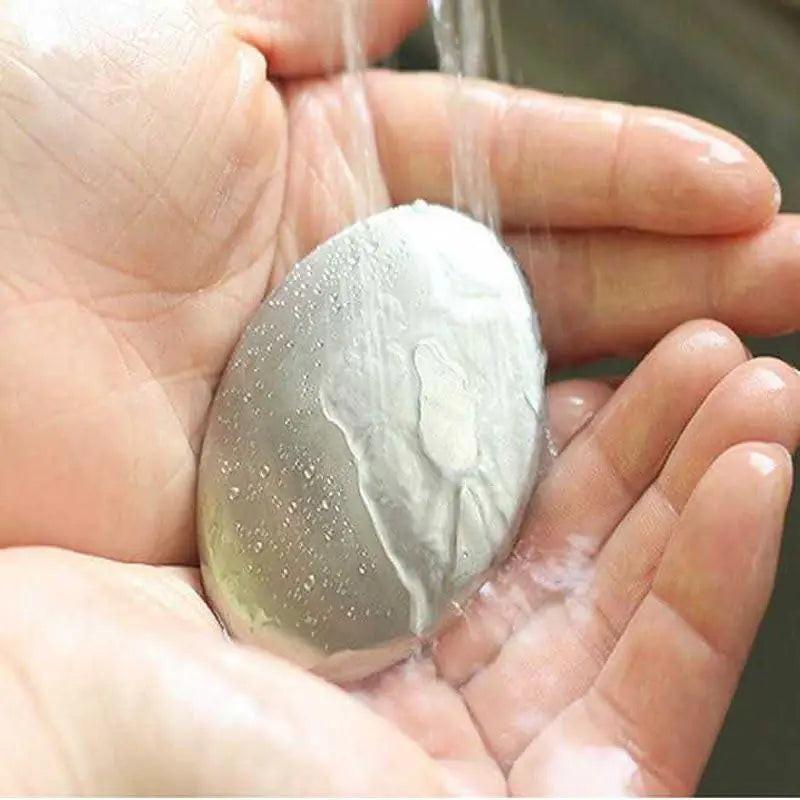 A person holds the Odor Remover Hand Bar Stainless Steel Soap under running water. This smooth, reflective bar is used to remove odors from hands and resembles a metallic soap bar.