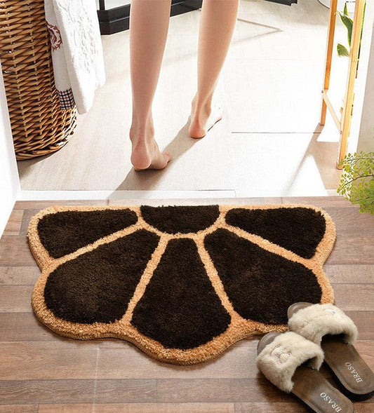 A person stands barefoot on a Supersoft Anti Skid Microfiber Doormat (45x70cms), featuring brown and beige petal patterns, placed on a wooden floor. Slippers are nearby, and sunlight enters through the doorway.